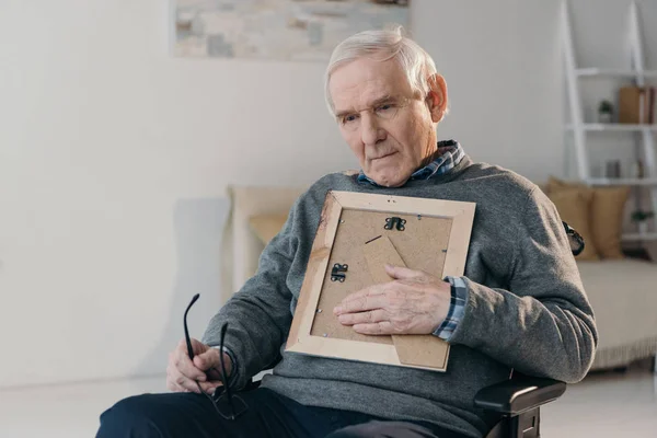 Nachdenklicher älterer Mann sitzt im Stuhl und hält alten Fotorahmen — Stockfoto