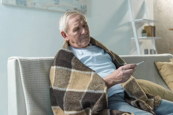 Hombre mayor comprobando la temperatura corporal con termómetro - foto de stock