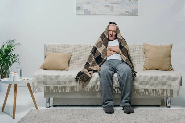 Senior homme réfrigéré couvert de plaid assis sur le canapé — Photo de stock