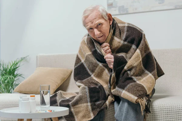 Senior chilled man covered in plaid with medications on table — Stock Photo