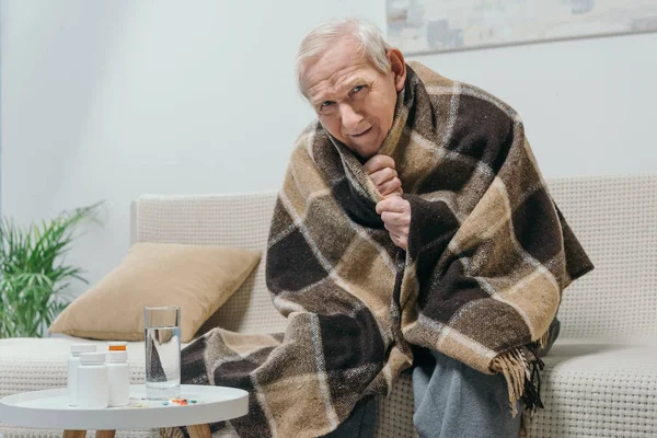 Hombre mayor refrigerado cubierto de cuadros con medicamentos en la mesa - foto de stock