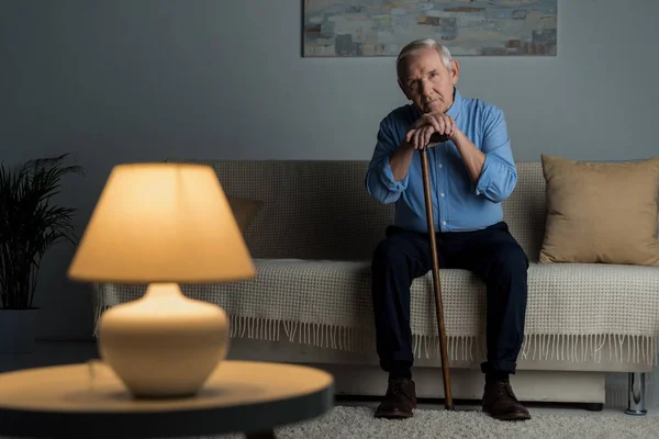 Tired senior man leans on a cane while sitting on sofa — Stock Photo