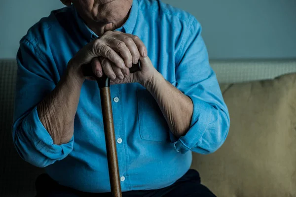 Close-up view of senior man leans on a cane while sitting on sofa — Stock Photo
