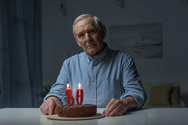 Senior lonely man celebrating 80 anniversary with cake and burning number candles — Stock Photo