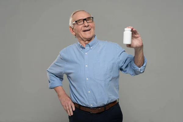 Un homme souriant âgé tient une bouteille blanche de pilules isolées sur fond gris — Photo de stock