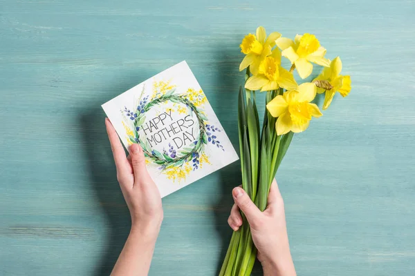 Card and daffodils in hands — Stock Photo