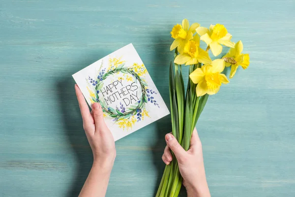 Cartão e narcisos nas mãos — Stock Photo