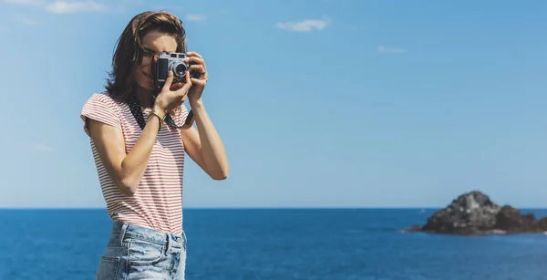 Tourist traveler photographer making pictures sea scape on vintage photo camera on background yacht and boat piar, hipster girl enjoying peak mountain and nature holiday, mockup ocean waves view, blurred backdrop