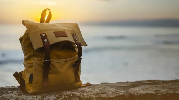 Hipster hiker tourist yellow backpack closeup on background blue sea enjoying sunset ocean horizon, blurred panoramic seascape sunrise blank mockup, traveler relax holiday concept, sunlight view in trip vacation