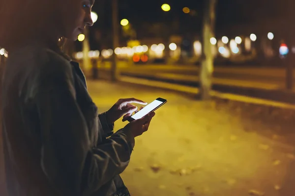 Woman pointing finger on screen smartphone on background illumination bokeh light in night atmospheric city, hipster using in hands mobile phone closeup, mockup glitter street in Barcelona, online wifi internet concept