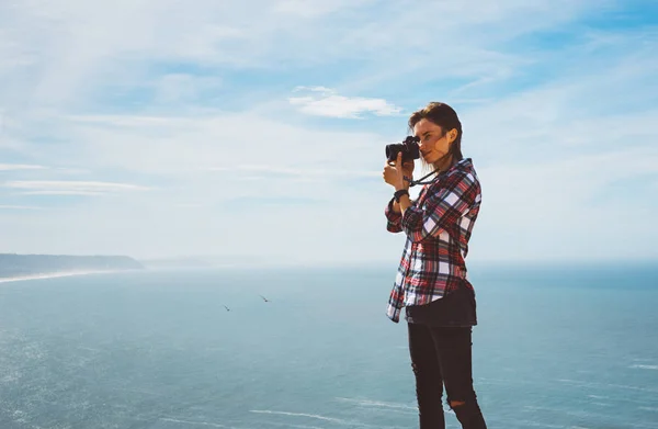 Tourist traveler photographer making pictures sea scape on photo camera on background ocean, hipster girl looking on nature horizon, relax holiday, blank space blue waves view, blurred backdrop for text