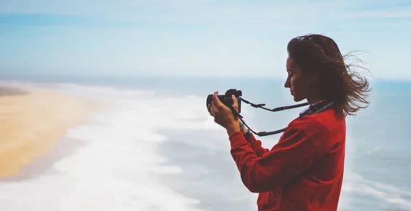 Tourist traveler photographer making pictures sea scape on photo camera on background ocean, hipster girl looking on nature horizon, relax holiday, blank space blue waves view, blurred backdrop for text