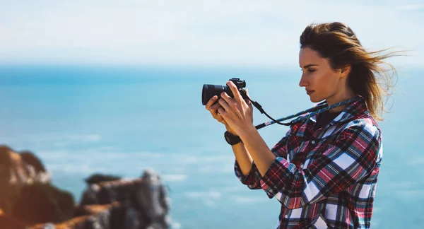 Tourist traveler photographer making pictures sea scape on photo camera on background ocean, hipster girl looking on nature horizon, relax holiday, blank space blue waves view, blurred backdrop for text
