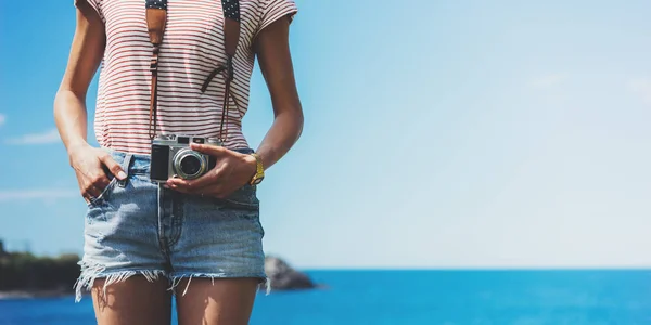 Tourist traveler photographer making pictures holding photo camera on background ocean sea scape, hipster girl looking on nature horizon, relax holiday, blank space blue waves view, backdrop for text