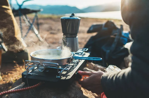 person cooking in nature camping outdoor, cooker prepare breakfast picnic on metal gas stove, hot tea outside; campsite lifestyle