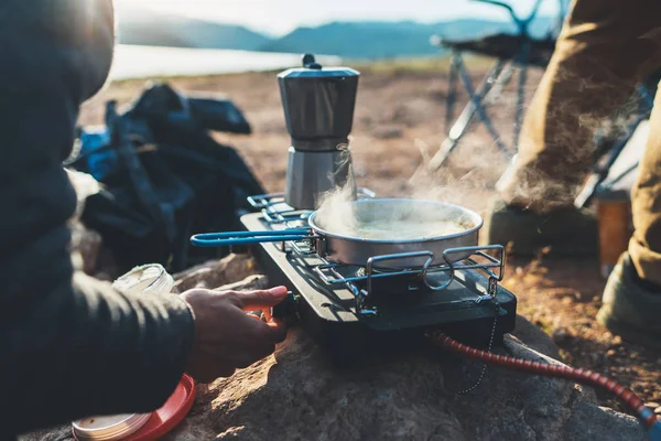 person cooking hot drinks in nature camping outdoor, cooker prepare breakfast picnic on metal gas stove, tourism recreation outside; campsite lifestyle