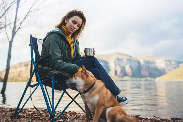 tourist traveler drink tea girl relax together dog on mountain scape,  woman hug pet rest on lake shore nature trip