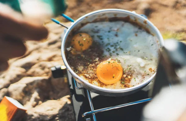 campsite lifestyle, person cooking fried eggs in nature camping outdoor, prepare scrambled omelette, breakfast picnic on metal stove