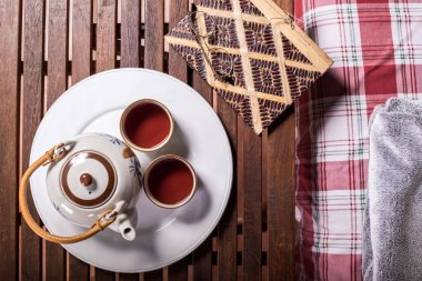 Tahta masada bir fincan çay ve üzerinde bardaklar olan bir kitap.