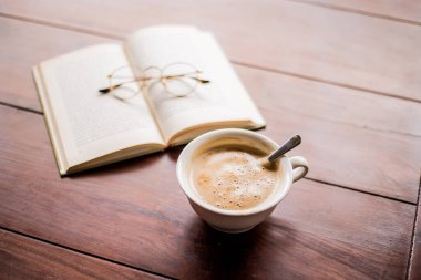 Arka planda kitap ve bardak olan bir fincan kahve.