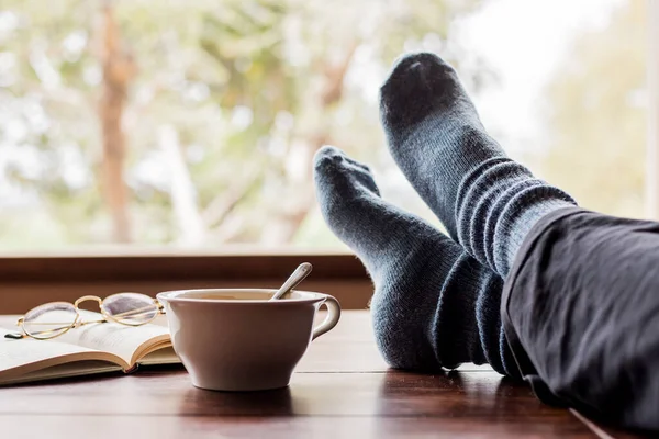 cup of coffee and a book with legs resting on a table