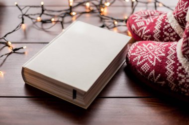 Beyaz kitap ve Noel ışıkları olan kırmızı çizmeler.