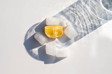 Buz küpleri arasında cam gölgeli bir parça limon.