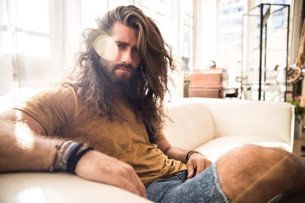 young man with long hair sitting, laying and standing on a sofa