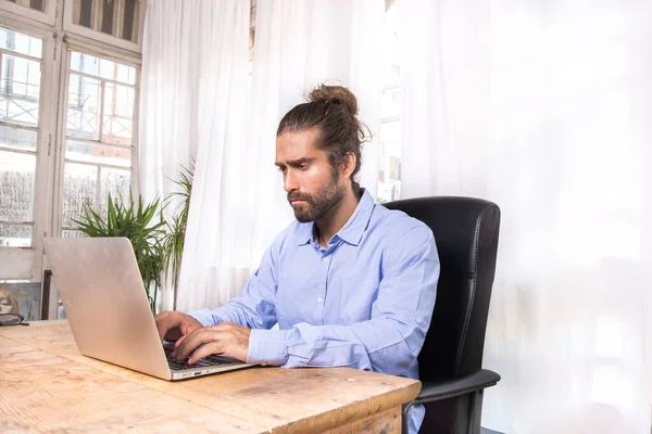 man with long hair working with his laptop in a office