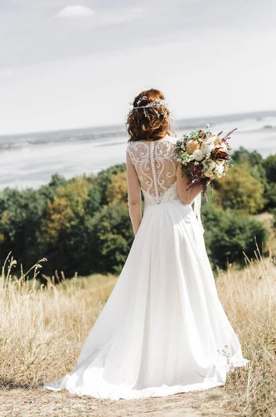Die Braut in einem weißen Kleid auf dem Gipfel des Berges zum Fluss verschüttet — Stockfoto