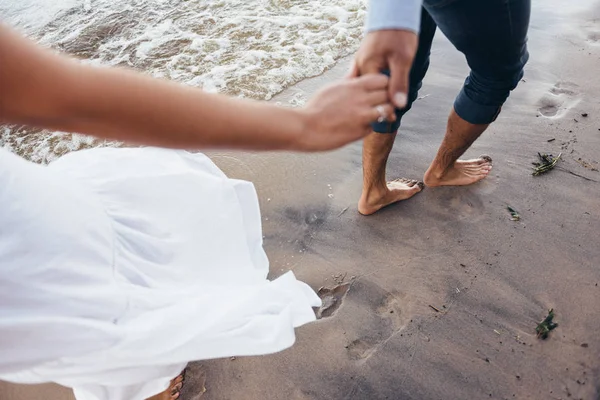 Cara segurando a mão de uma menina, levando-a ao longo da areia molhada no — Fotografia de Stock