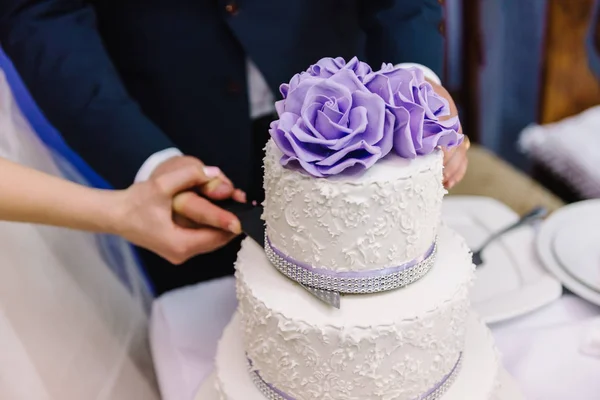 Cutting wedding cake with purple flowers