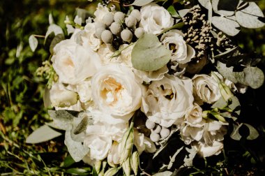 Gelinin beyaz gül ve şakayık buketi güneşli bir günde yeşil çimlerin üzerinde yatıyor.