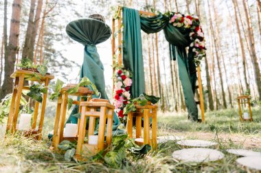 Yeni evliler için tören kemerinin arka planında güneşli bir orman zemininde yeşil çimlerin olduğu bir düğün dekorunun ayrıntıları.
