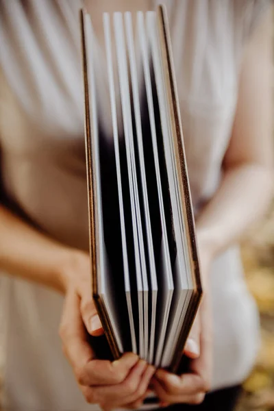 premium photo book album for wedding photography with a wooden cover and a leather spine in the hands of a girl on a blurred background of a green park