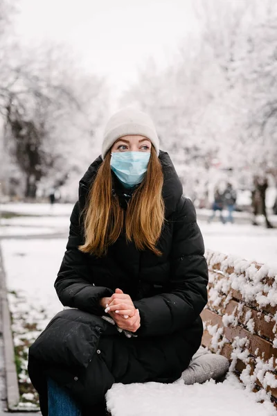 ウイルスとインフルエンザの滅菌医療マスクの少女が公園のベンチに座っています 冬の日 寒いわね — ストック写真