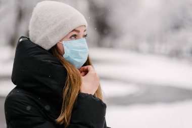 Virüslerden dolayı steril tıbbi maske takan bir kız ve grip kendinden uzak görünüyor. Mesaj için yer. Beyaz bulanık arka plan. Kar yağıyor. Kötü hava