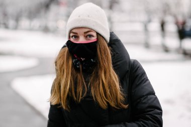 Virüslerden siyah maskeli bir kız ve çiçekli bir grip karlı bir günde sokakta yürüyor.