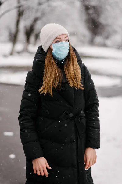 ウイルスの滅菌医療マスクの少女は 全長の公園の空の路地に立っています 外は湿っていて雪が降っている — ストック写真