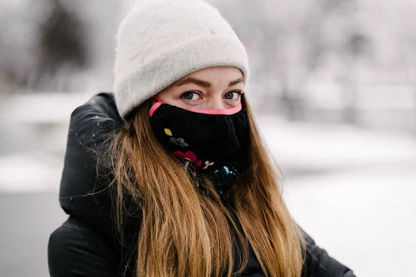 雪の日にデザイナーの黒いマスクの女の子と花のインフルエンザが通りを歩いています — ストック写真