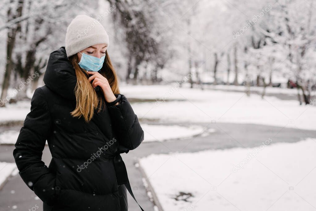 A girl in a sterile medical mask protects against the flu virus outdoors on a wet and wet snowy day