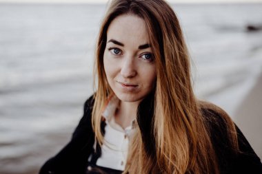 Okyanusta siyah elbiseli üzgün bir kızın portresi rüzgarda gelişen saçları ve ellerinde kuru otlarla huş ağacında yuvarlanan dalgalar. Bulanık arkaplan