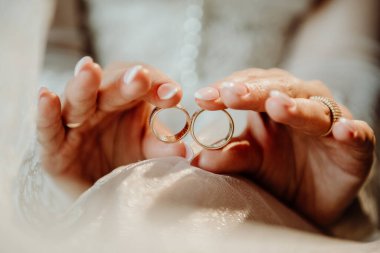 Gelinin elinde iki altın yüzük var. Beyaz bir duvağın üzerinde ve bulanık bir geçmişi var. Gelinin ellerinde çok güzel, pahalı bir altın yüzük var.