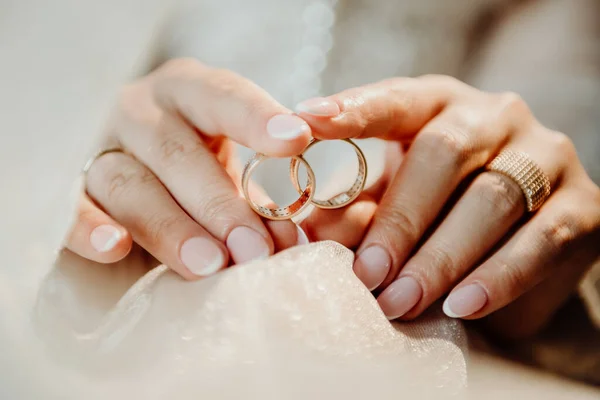 Két Arany Gyűrű Menyasszony Kezében Fehér Esküvői Fátylon Homályos Háttérrel — Stock Fotó