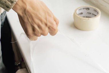 Bir işçi pencere pervazından plastik filmi kaldırır.