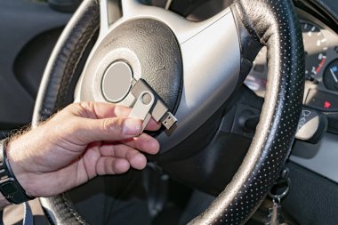 Adamın biri elinde flaş bellek tutuyor ve arabada oturuyor.