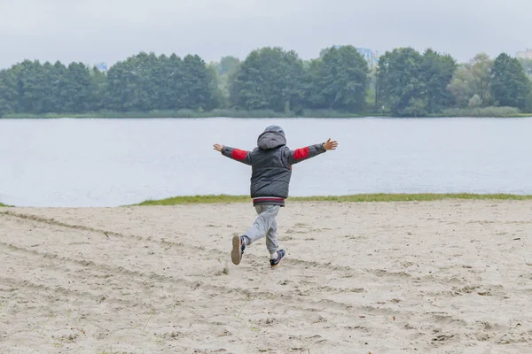 A little boy walks alone on the river Bank in autumn