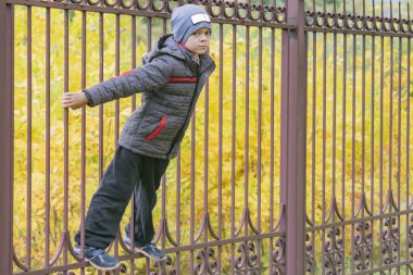 Küçük bir çocuk sonbahar bahçesinde çitin yanında yürüyor.