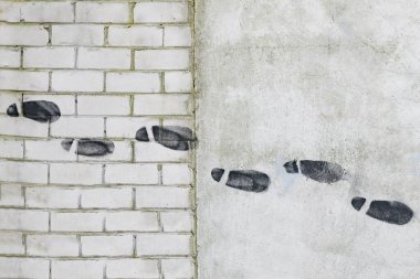 Beton duvardaki ayak izleri siyah boyayla çizilmiş.
