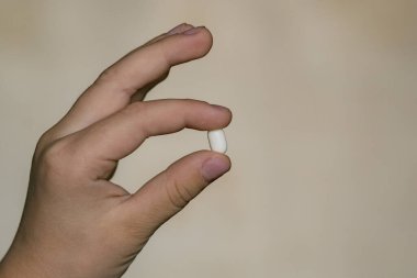 Küçük bir çocuk elinde beyaz bir hap tutuyor.